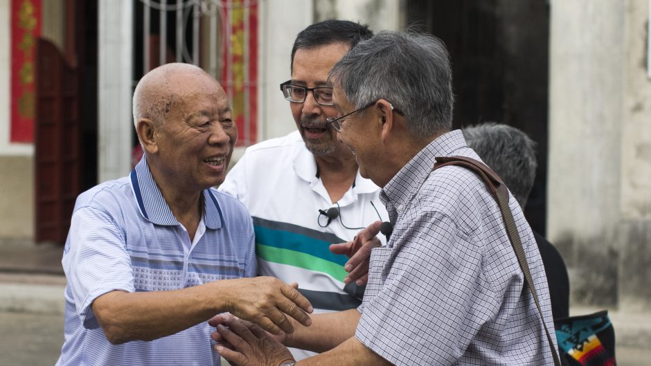 A screenshot from the film All our Father's Relations. Three Chinese men are happy to see each other.