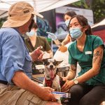 A veterinarian talks to a man while she cares for his dog.