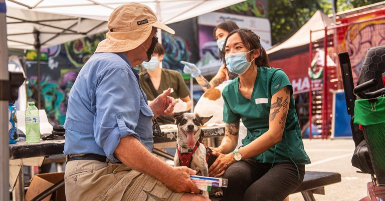 A veterinarian talks to a man while she cares for his dog.